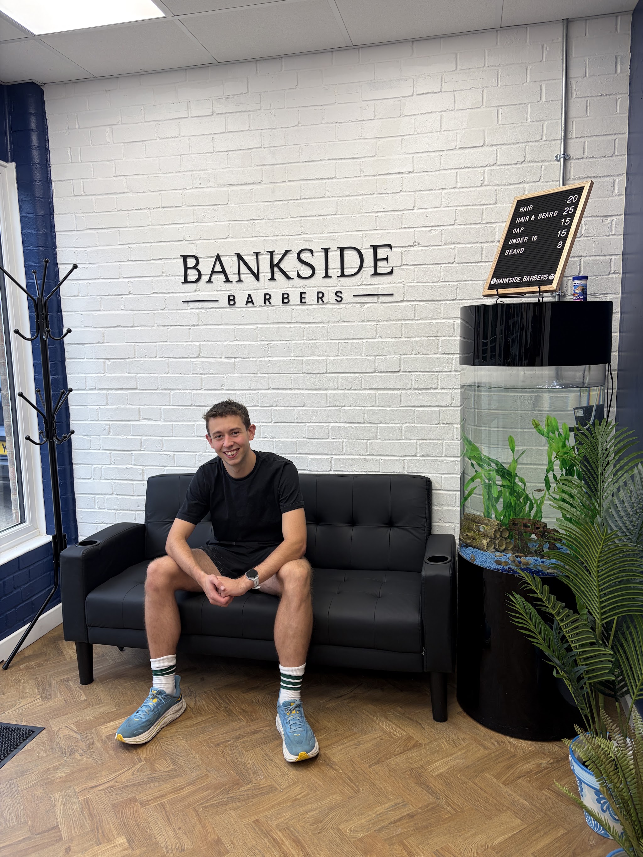Zach Dale on the leather sofa under the Bankside Barbers wall sign
