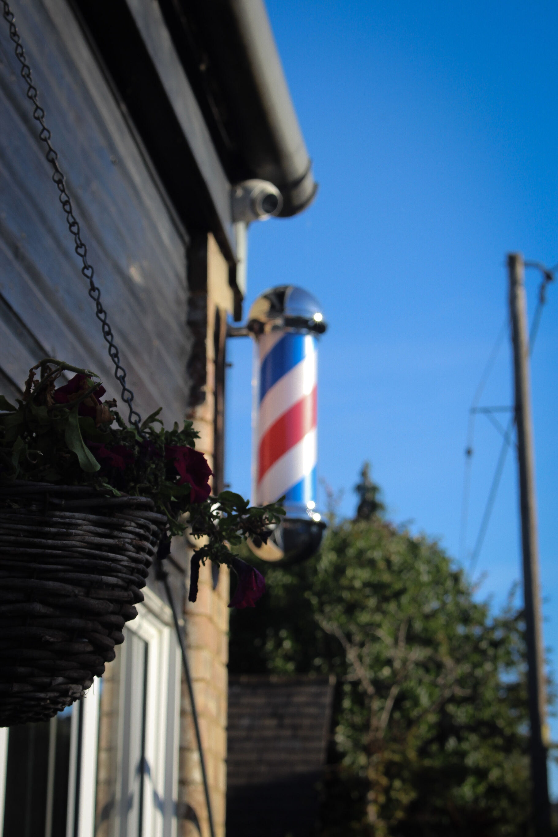 Red, white and blue barber pole beside a hanging basket